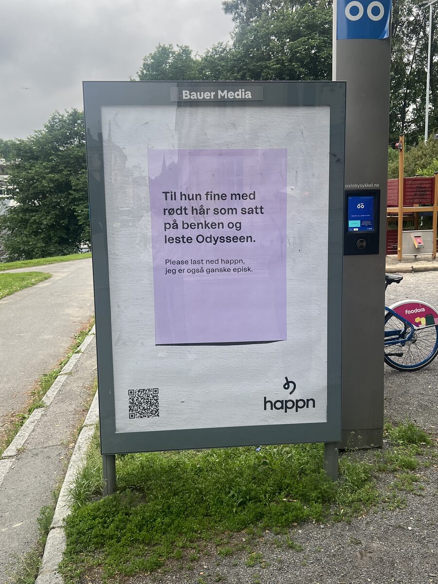 Lilla Happn-plakat på en reklametavle ved en sti: Til hun fine med rødt hår som satt på benken og leste Odysseen